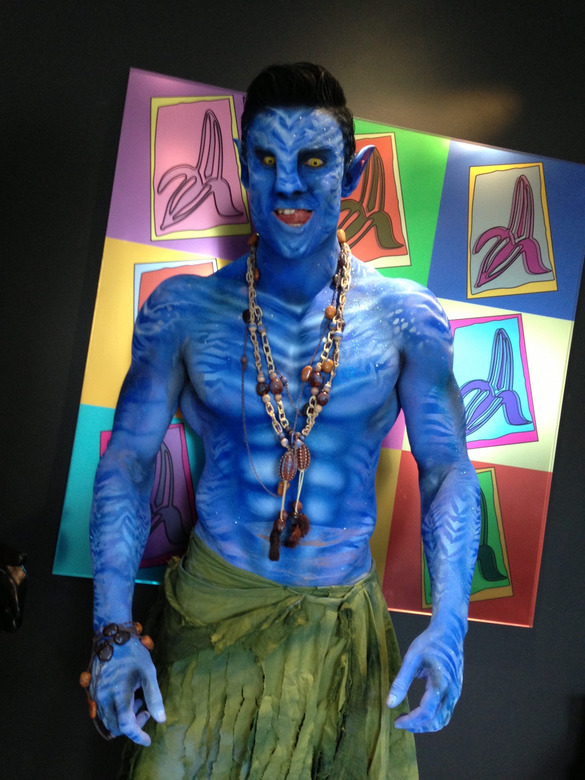 Male fitness model and performer body painted with airbrush and prosthetics blue as an avatar avi at banana split plc offices London