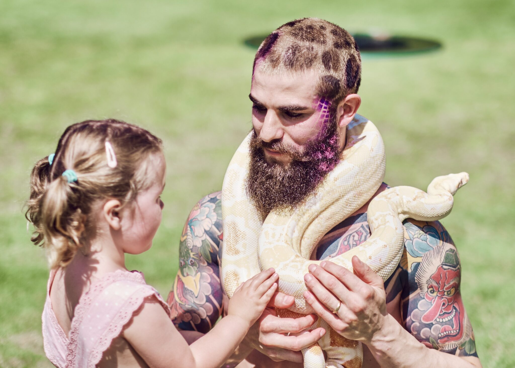 Snake Charmer A young girl strokes a snake around the neck of a circus performer covered with fantastical coloured tattoos