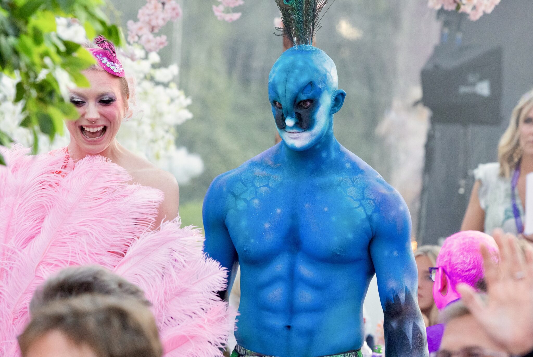 The Flamingo and The Peacock A toned male circus performer body painted with prosthetics and feathered headdress as a peacock at a summer garden party on a private estate